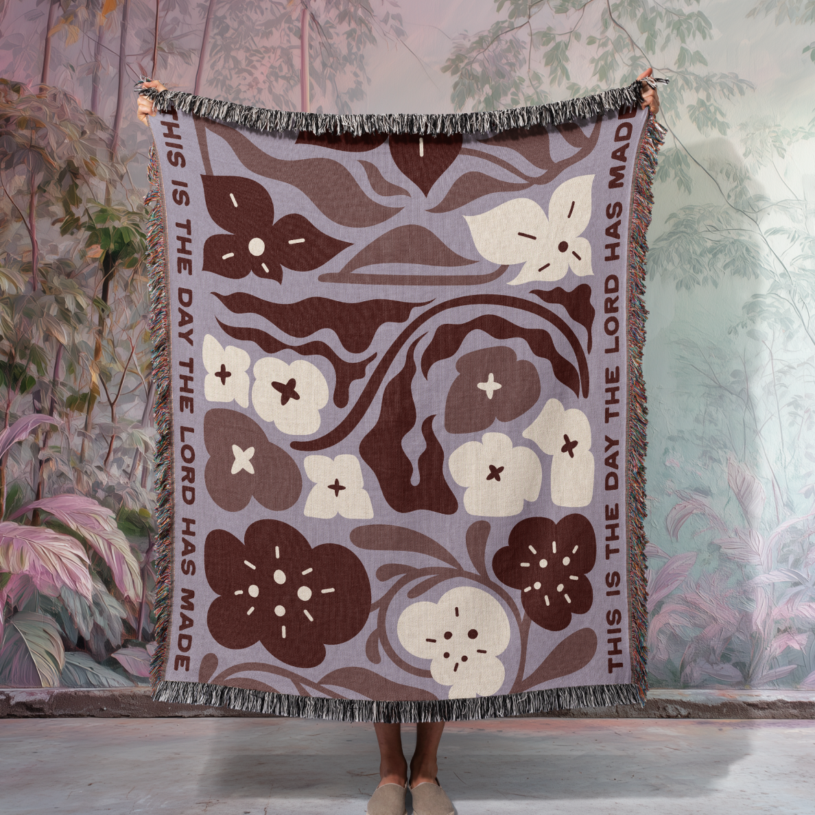 Floral patterned blanket with text held by a person against a nature-themed wall.