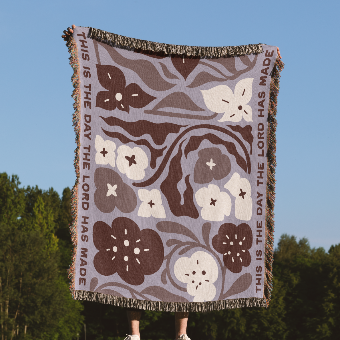 Floral patterned blanket with text against a blue sky and green trees background