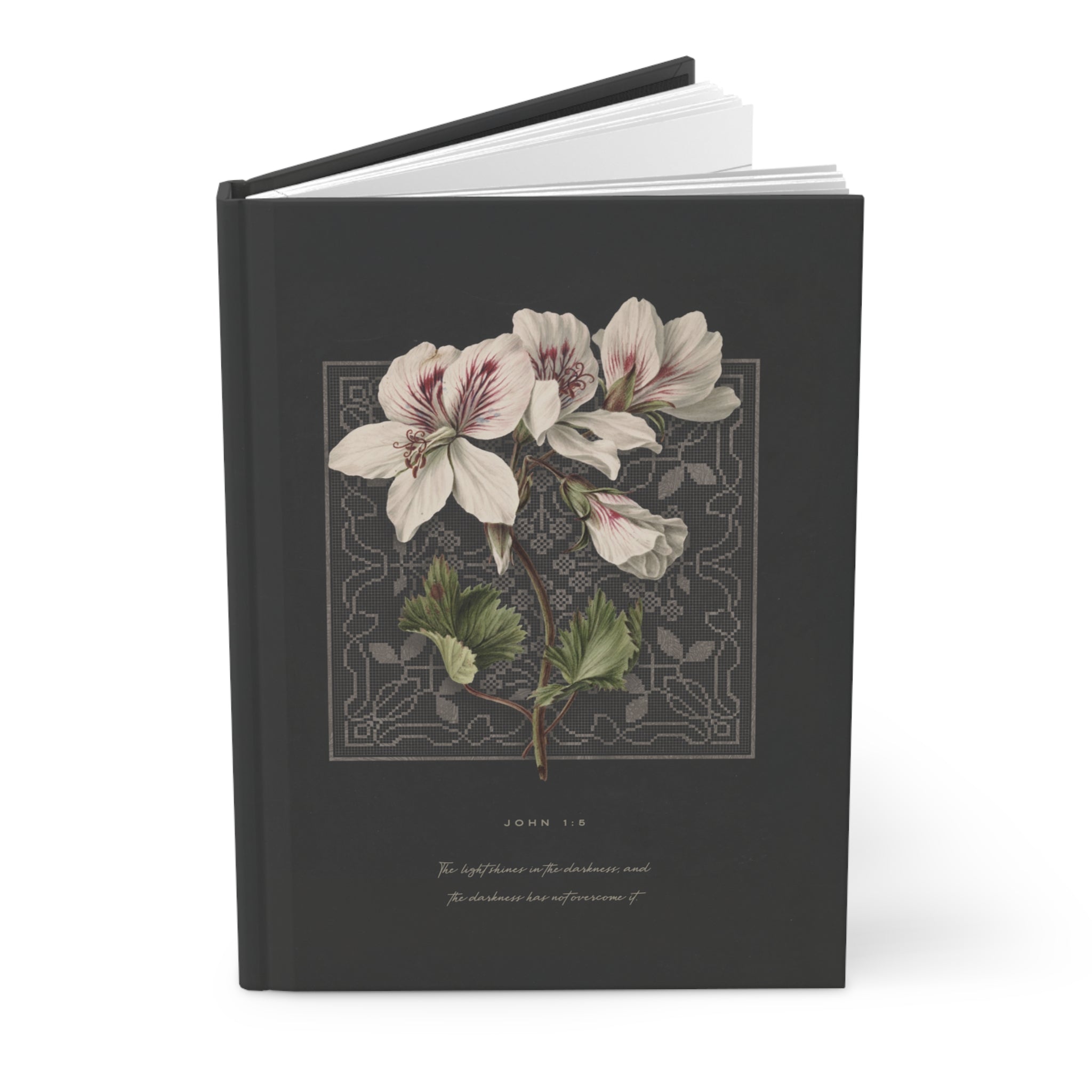 A hardcover journal or book with a dark charcoal-gray cover, featuring a vintage botanical illustration of white flowers with green leaves and a gray ornamental border. The title 'JOHN 1:18' and a subtitle are printed in light gray text below the illustration.