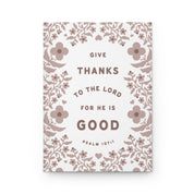 Notebook with floral design and text 'Give thanks to the Lord for he is good' on a white background