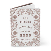 Notebook with floral design and text 'Give thanks to the Lord for he is good' on a white background