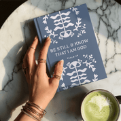 Book titled 'Be Still & Know That I Am God' on a marble surface with a hand holding it.