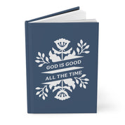 Blue book with white floral design and 'God is Good All the Time' text on a white background