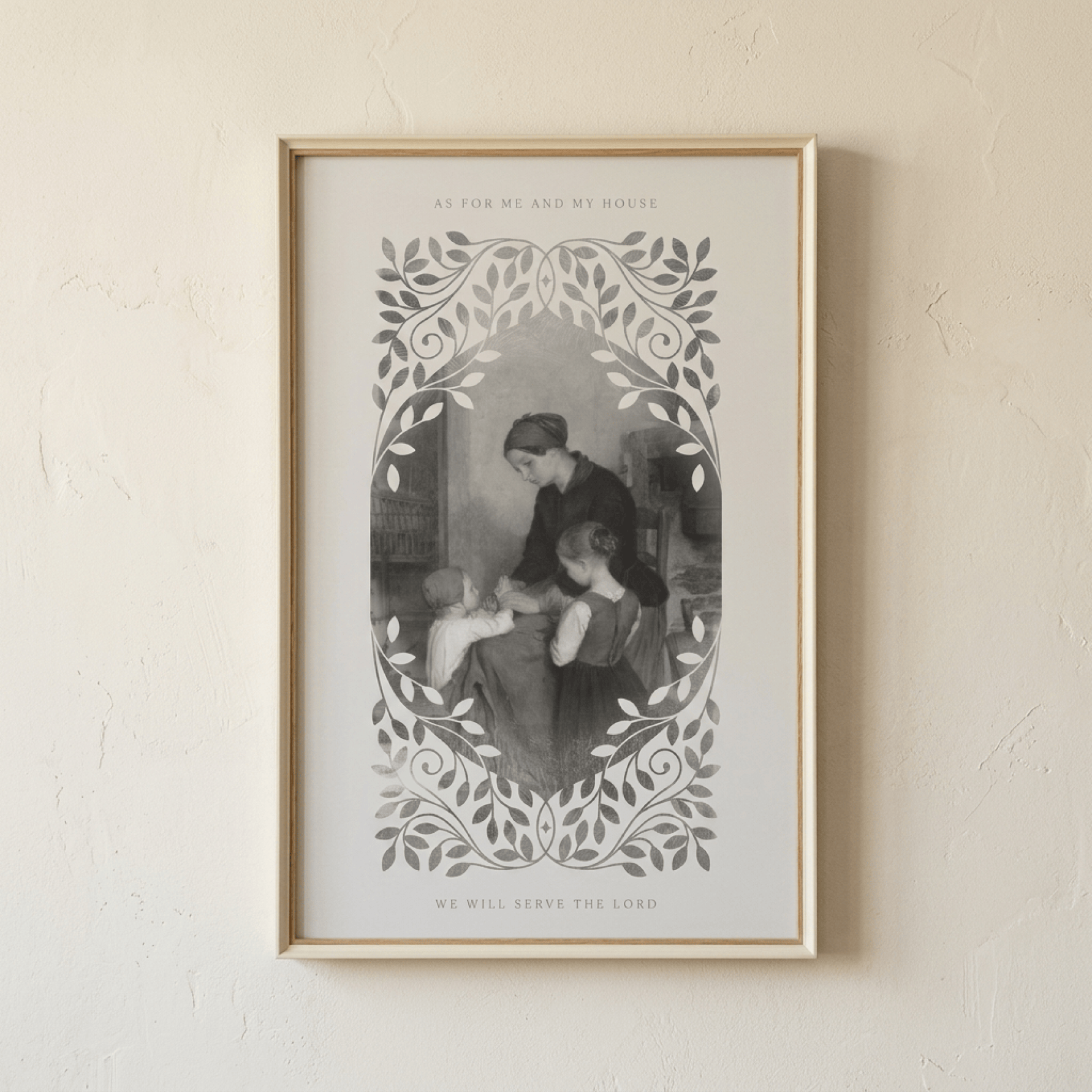 A framed art print featuring a vintage black and white illustration of a mother and child, surrounded by a decorative leafy border, hanging on a textured beige wall.