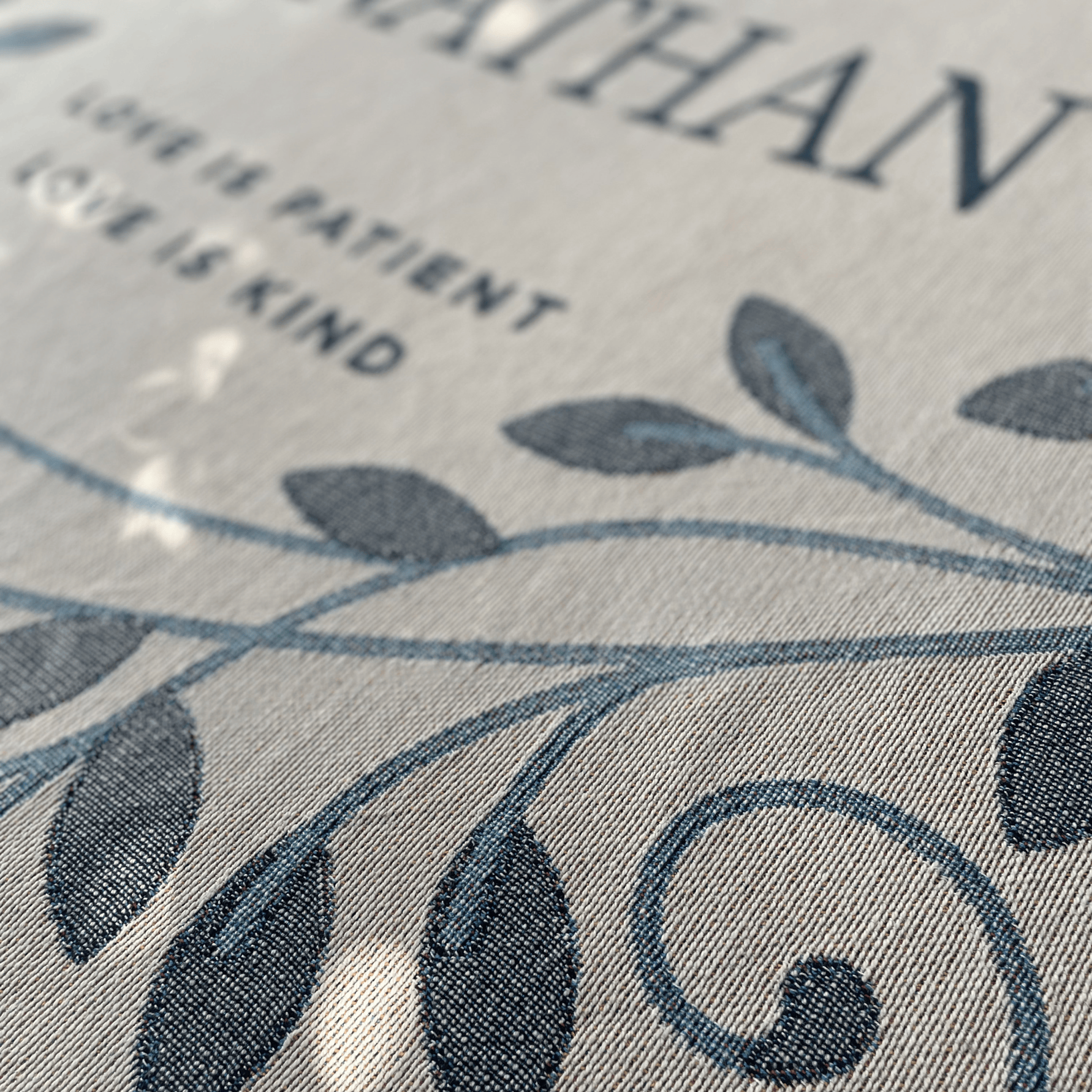 Textured fabric with leaf pattern and text 'LOVE IS PATIENT AND KIND' on a gray background