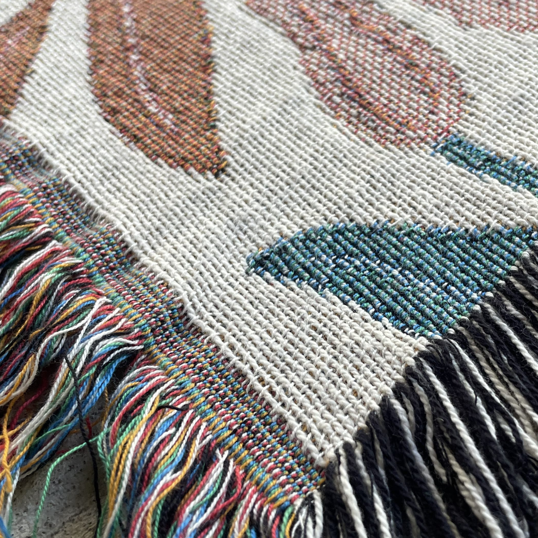 Close-up of a woven textile with colorful patterns and fringes.