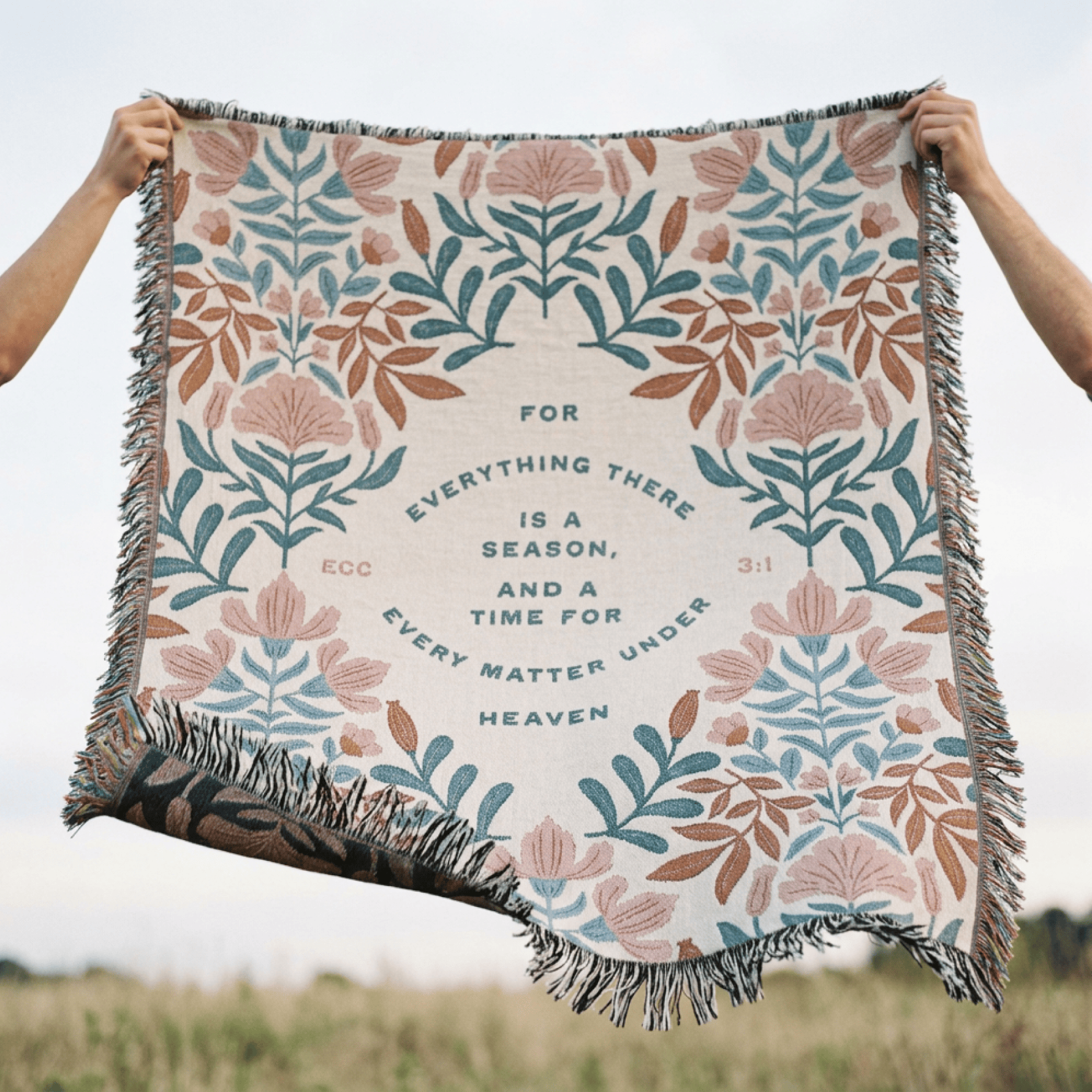 Floral patterned blanket with text held up against a field background