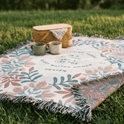 Floral-patterned picnic blanket with a woven basket and mugs on grass