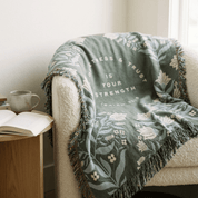 Christian woven blanket with Isaiah 30:15 botanical pattern draped over white armchair in living room