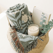 In Quietness and Trust woven blanket folded in wicker basket with candle on white surface