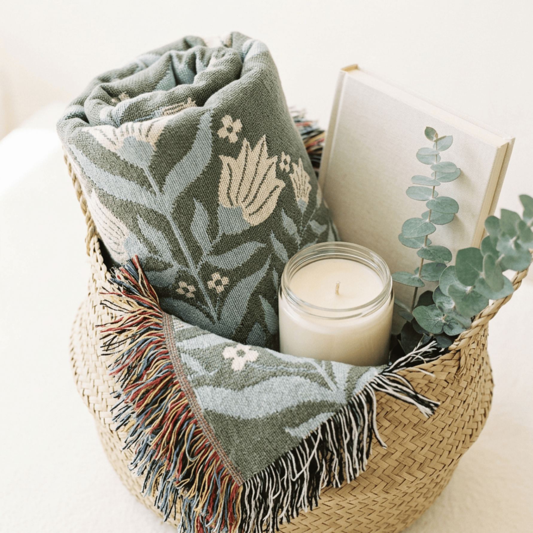 In Quietness and Trust woven blanket folded in wicker basket with candle on white surface