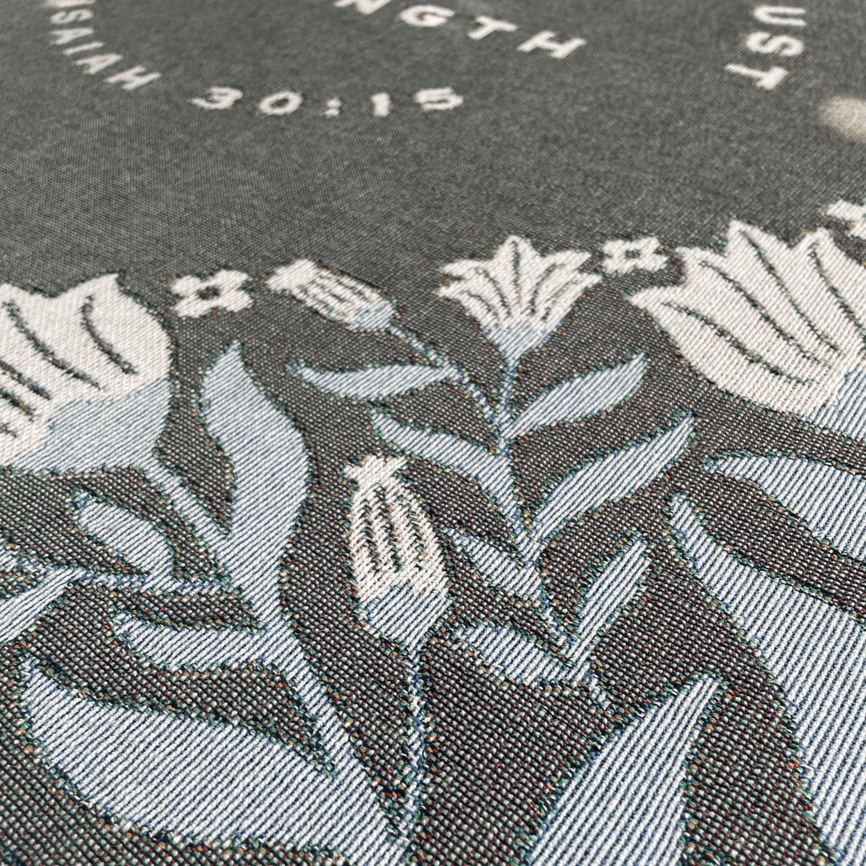 Close-up of In Quietness and Trust text woven into sage green blanket fabric

