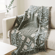 Sage green religious throw blanket draped over chair in natural light
