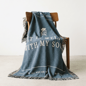 Blue blanket with text and a flower design draped over a wooden chair on a light background