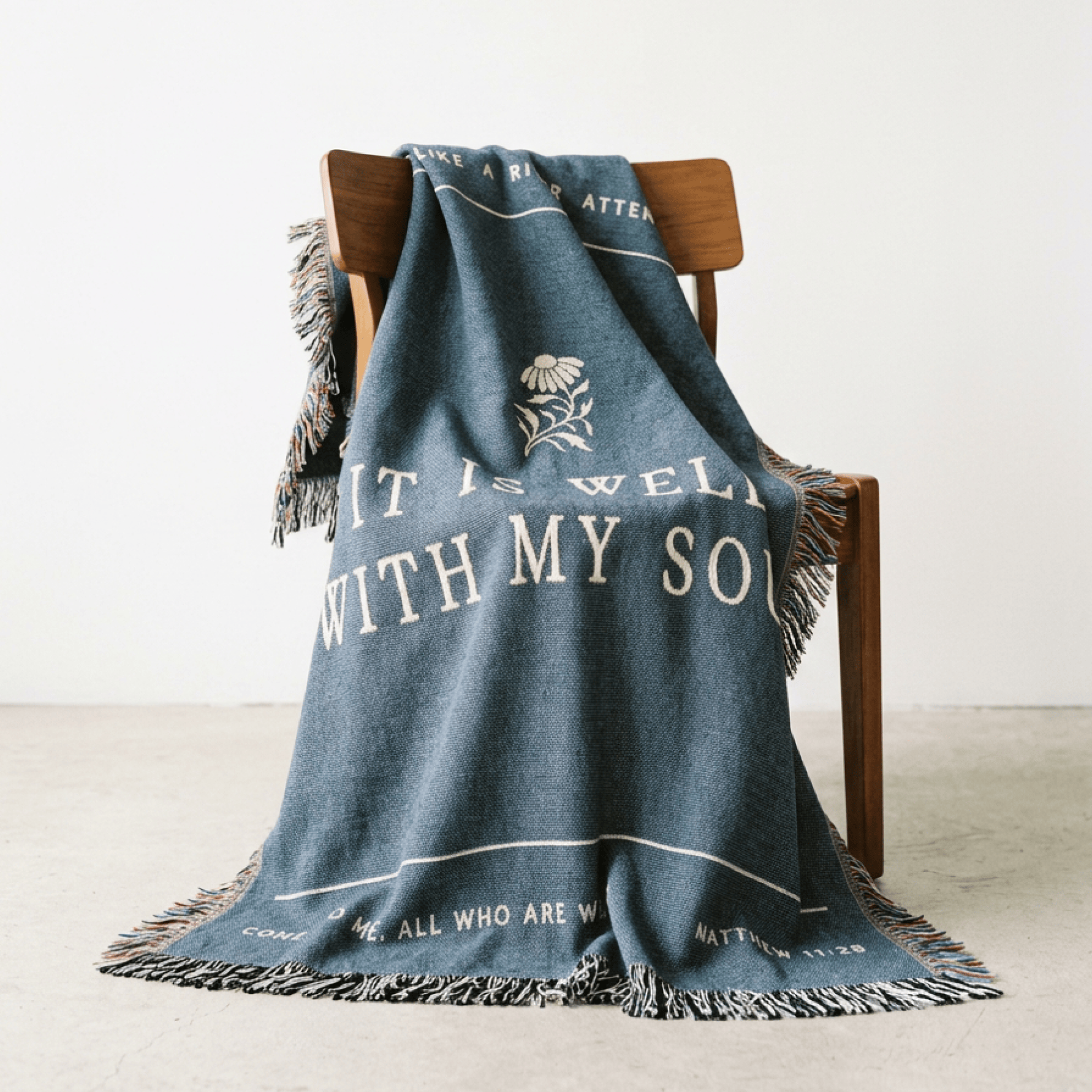 Blue blanket with text and a flower design draped over a wooden chair on a light background