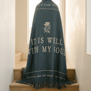 Blue prayer shawl with text and floral design draped over a wooden surface.