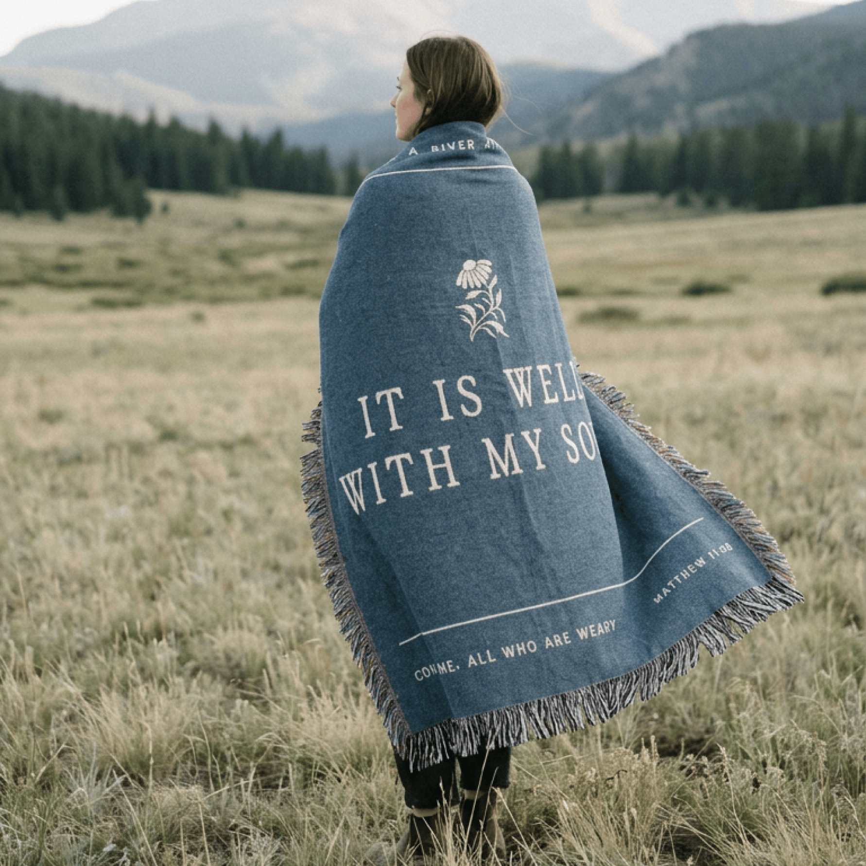 Person wrapped in a blue blanket with text in a field with mountains in the background
