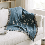 Blue throw blanket with 'It is well with my soul' text on a white couch.