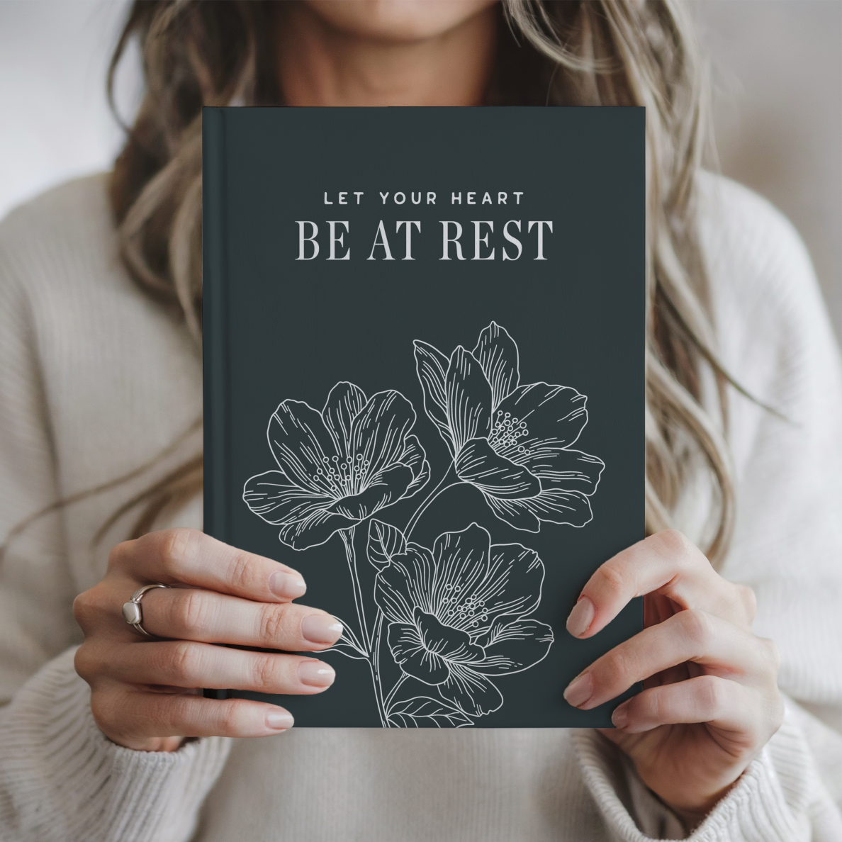 Person holding a book titled 'Let Your Heart Be at Rest' with floral illustrations.