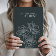 Person holding a book titled 'Let Your Heart Be at Rest' with floral illustrations.