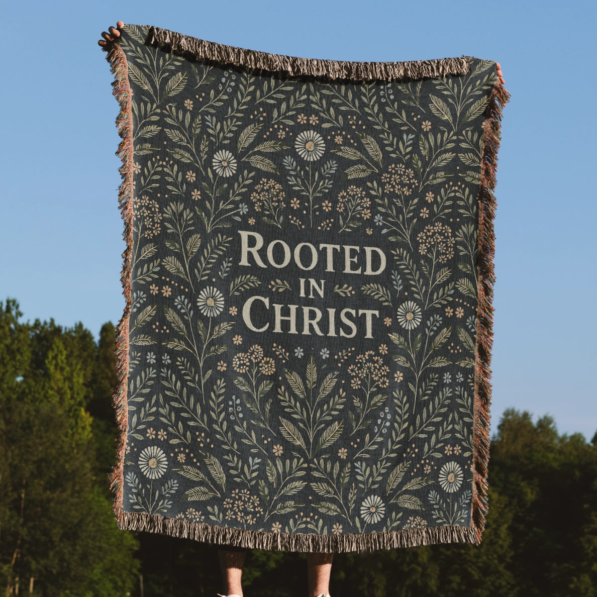 Faith-inspired woven blanket with floral patterns and the phrase “Rooted in Christ,” made from soft cotton—Christian home decor and gift.