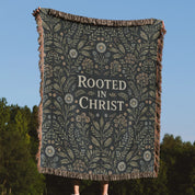 Faith-inspired woven blanket with floral patterns and the phrase “Rooted in Christ,” made from soft cotton—Christian home decor and gift.
