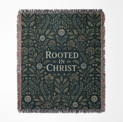 Faith-inspired woven blanket with floral patterns and the phrase “Rooted in Christ,” made from soft cotton—Christian home decor and gift.