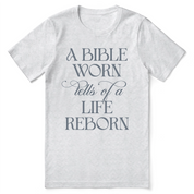 Christian t-shirt with the phrase “A Bible Worn Tells of a Life Reborn”; unisex cotton tee celebrating transformation through God's Word.