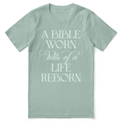 Christian t-shirt with the phrase “A Bible Worn Tells of a Life Reborn”; unisex cotton tee celebrating transformation through God's Word.
