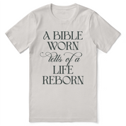 Christian t-shirt with the phrase “A Bible Worn Tells of a Life Reborn”; unisex cotton tee celebrating transformation through God's Word.