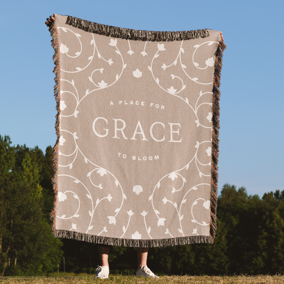 Blanket with 'A Place for Grace to Bloom' text and floral patterns in a natural setting