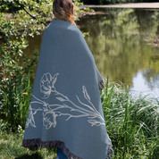 Person wrapped in a blue floral-patterned blanket by a pond