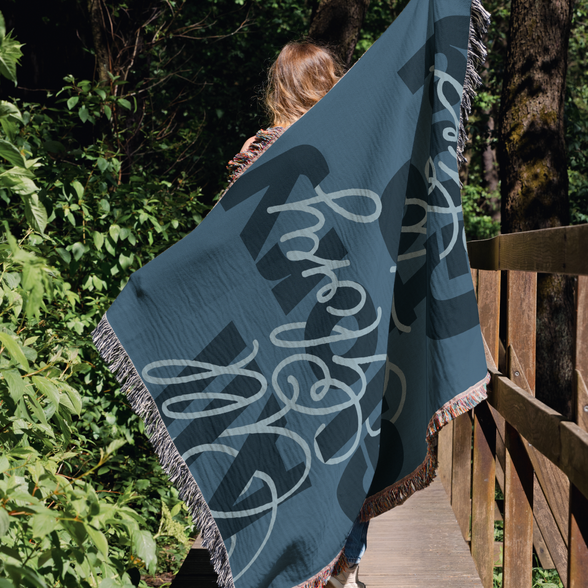 Person holding a blue blanket with white text in a forest setting