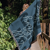 Person holding a blue blanket with white text in a forest setting
