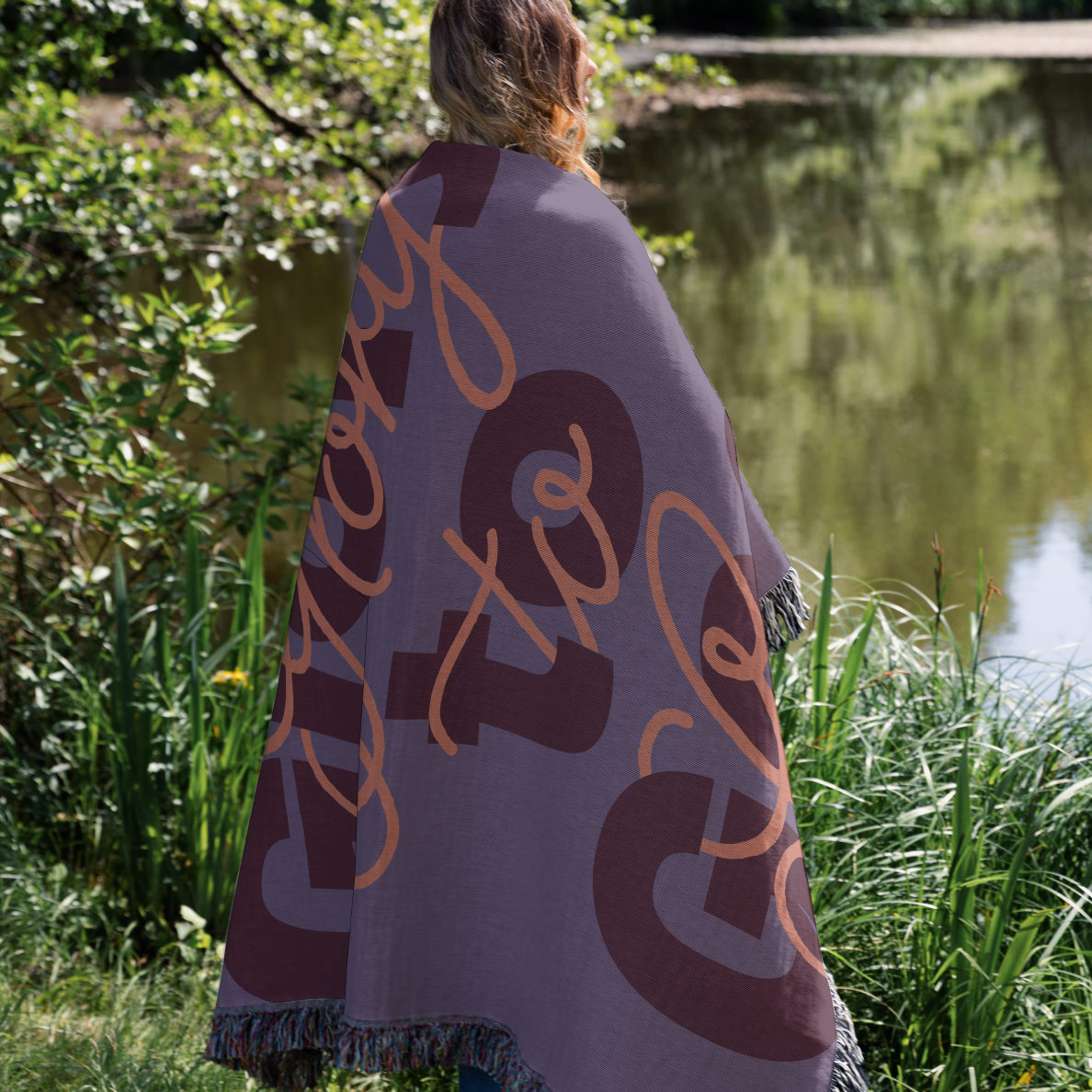 Person wrapped in a blanket with text standing by a body of water