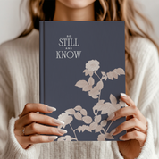 Person holding a book titled 'Be Still and Know' with floral design