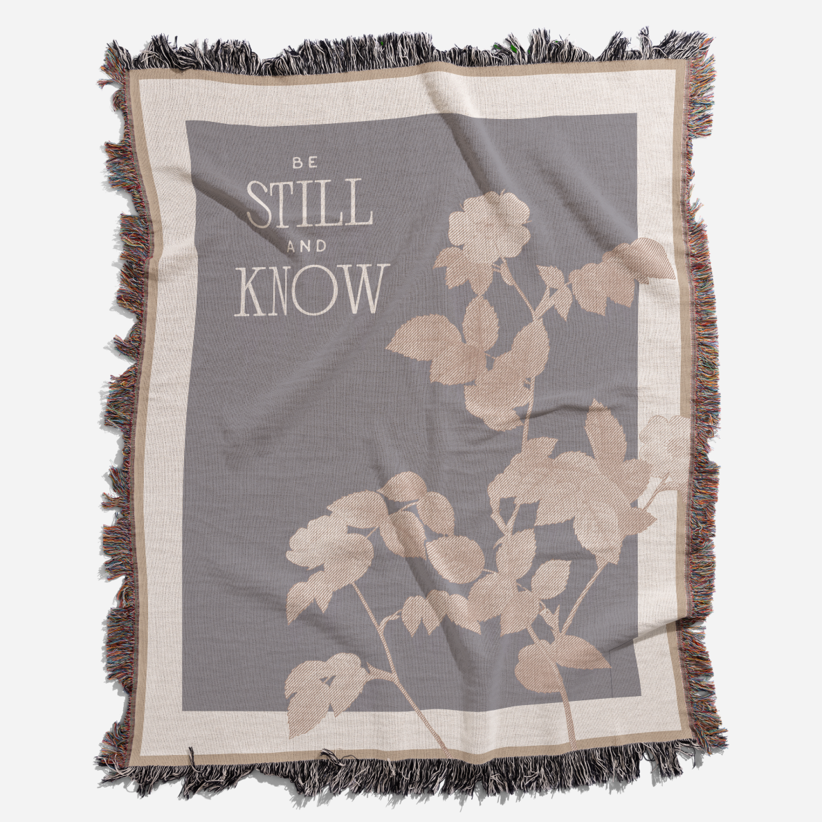 Blanket with floral design and 'Be Still and Know' text on a gray background