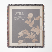 Blanket with floral design and text 'Be Still and Know' on a gray background
