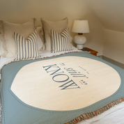 Round rug with 'Be Still and Know' text on a bed in a bedroom setting.