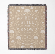 Cream-colored woven blanket with the phrase “Be still and know” from Psalm 46, made of 100% cotton with fringe; a peaceful Christian gift for nurseries or weddings.