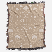 Cream-colored woven blanket with the phrase “Be still and know” from Psalm 46, made of 100% cotton with fringe; a peaceful Christian gift for nurseries or weddings.