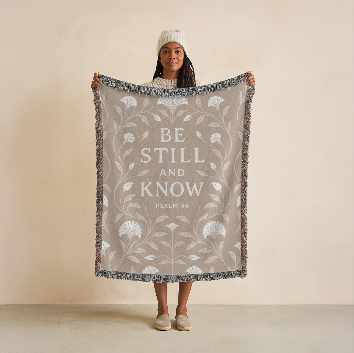 Cream-colored woven blanket with the phrase “Be still and know” from Psalm 46, made of 100% cotton with fringe; a peaceful Christian gift for nurseries or weddings.