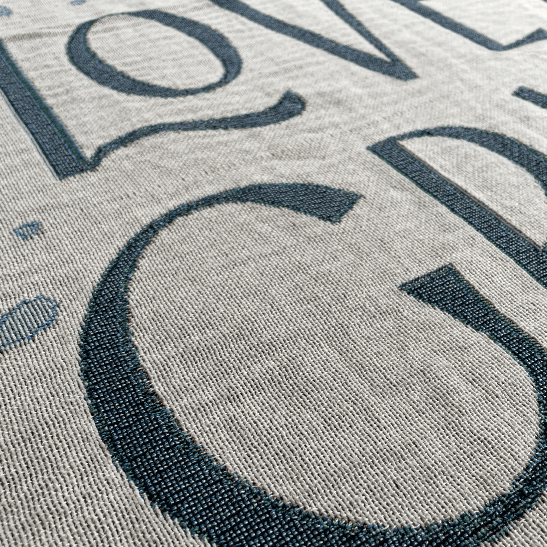 Close-up of a woven textile with large dark navy lettering on a light beige background.