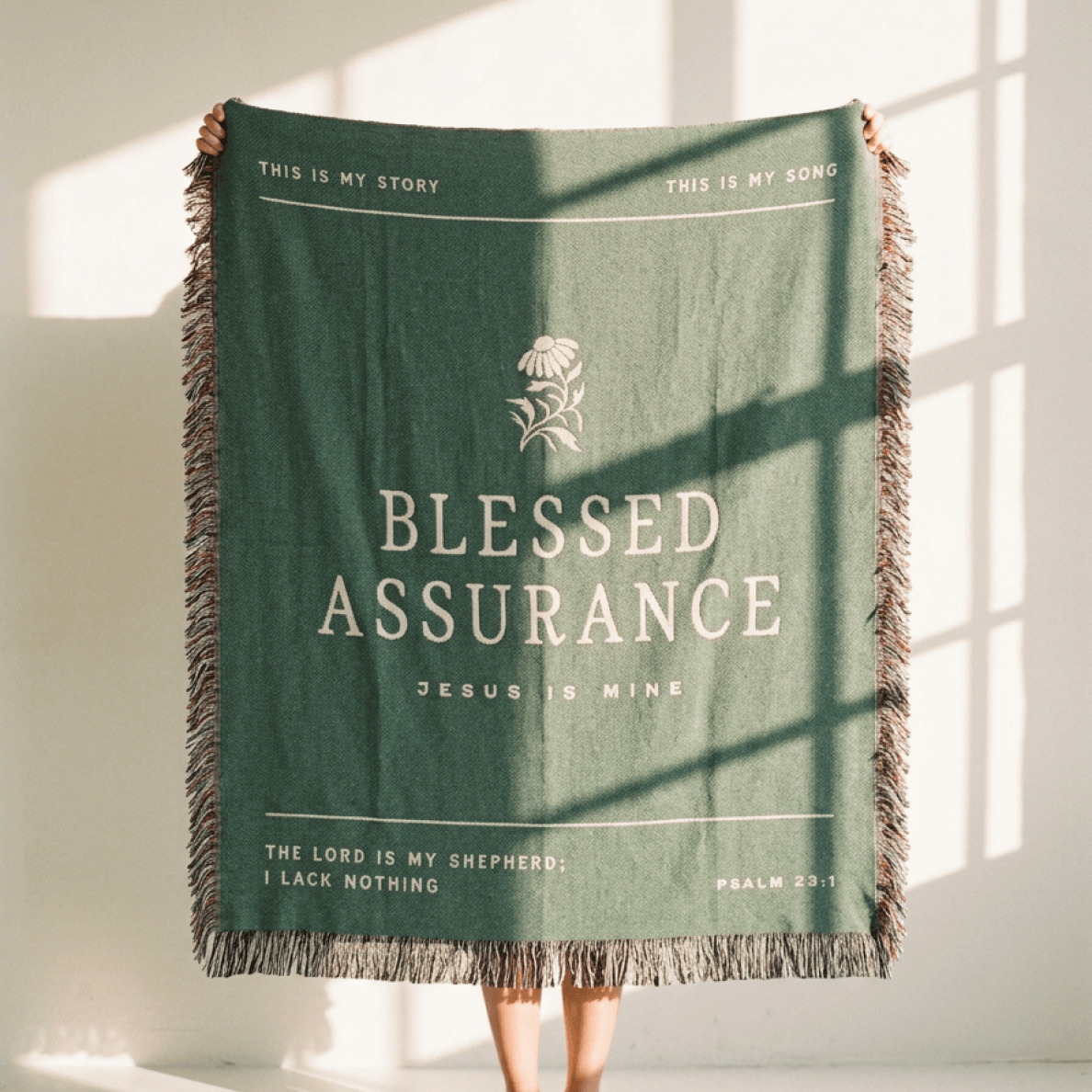 Green blanket with text and fringes, held by a person in a bright room.