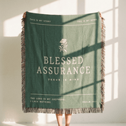 Green blanket with text and fringes, held by a person in a bright room.