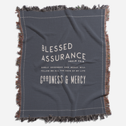 Gray blanket with text 'Blessed Assurance' and 'Goodness & Mercy' on a white background