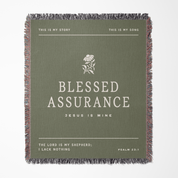 Green blanket with text and floral design, featuring the phrase 'Blessed Assurance'.