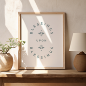 Framed artwork with 'Blessings Upon Blessings' text on a wooden shelf with decor items.