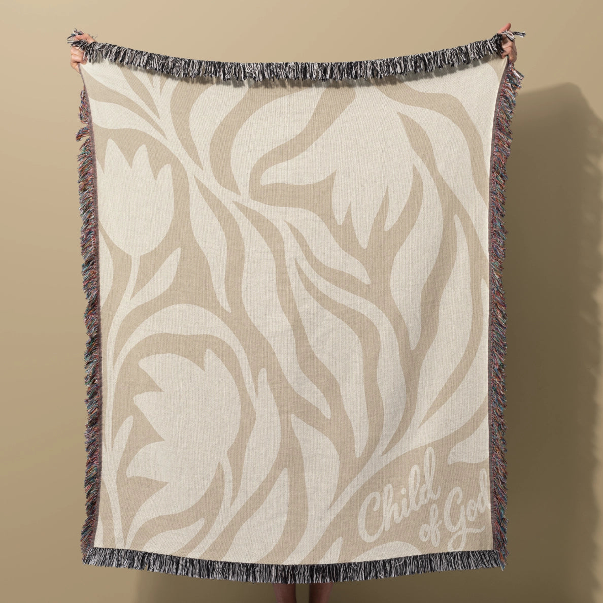 Neutral-toned woven blanket with “Child of God” text and delicate cream foliage design; 100% cotton with fringe, perfect for nurseries, baby gifts, or faith-inspired décor.