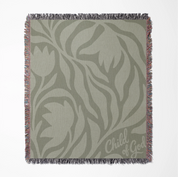 Green earthy-toned woven blanket with foliage pattern and “Child of God” text; made of 100% cotton with fringe, ideal for nurseries, kids’ rooms, or Christian gifts.